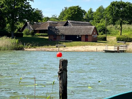 Das Haus am See Mustin am Kleinen See, umgeben von Schilf und Bäumen.